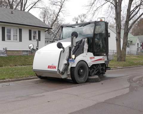 A street sweeper cleaning the gutters of a residential neighborhood street.